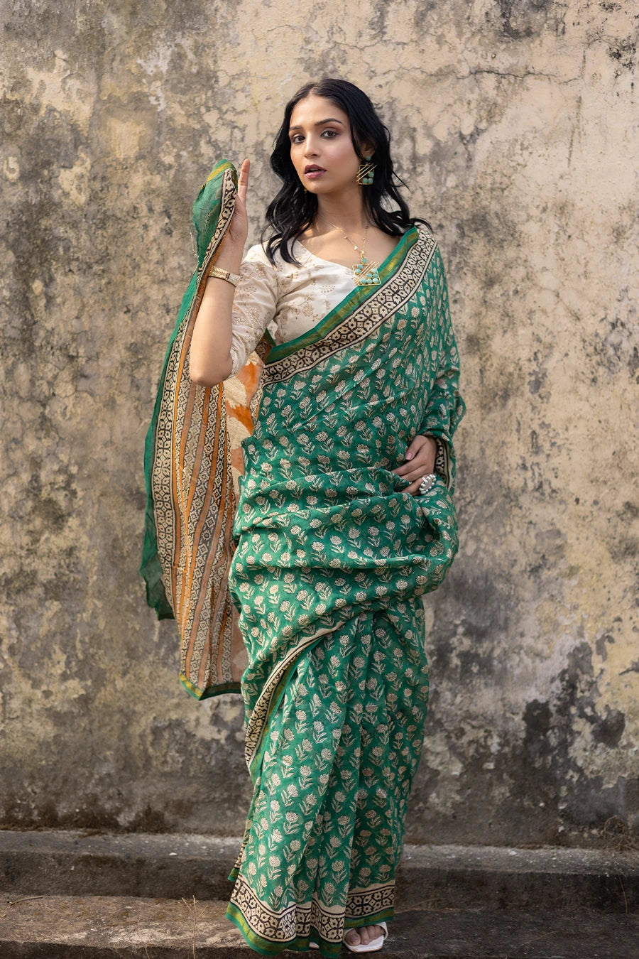 Woman in a green saree with a textured wall background