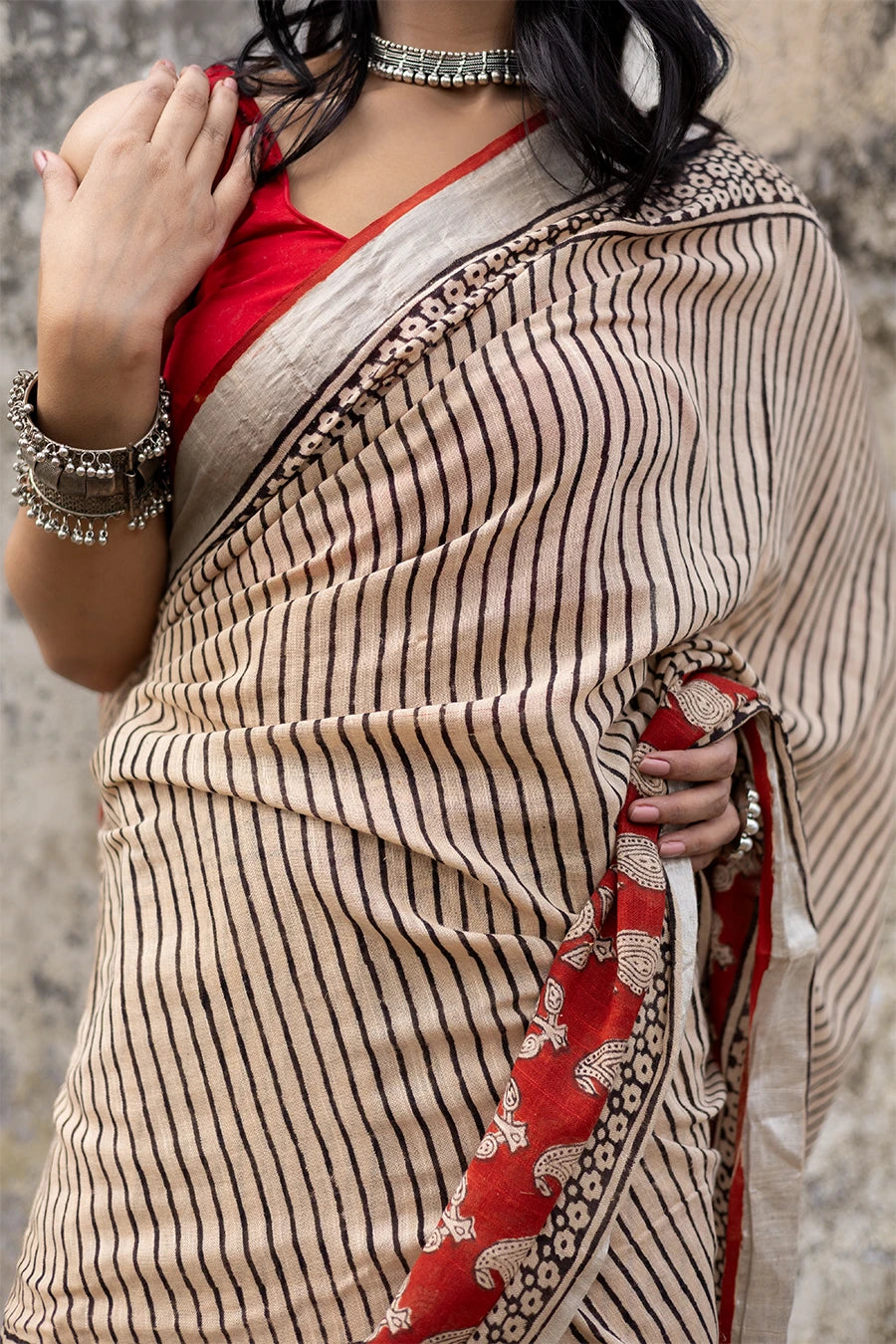 Woman in a red and beige saree standing on steps with a textured wall background