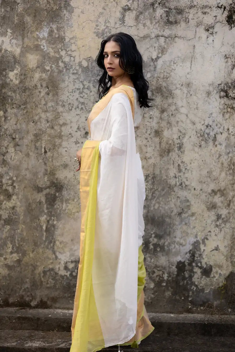 Woman wearing a white and yellow saree against a textured wall