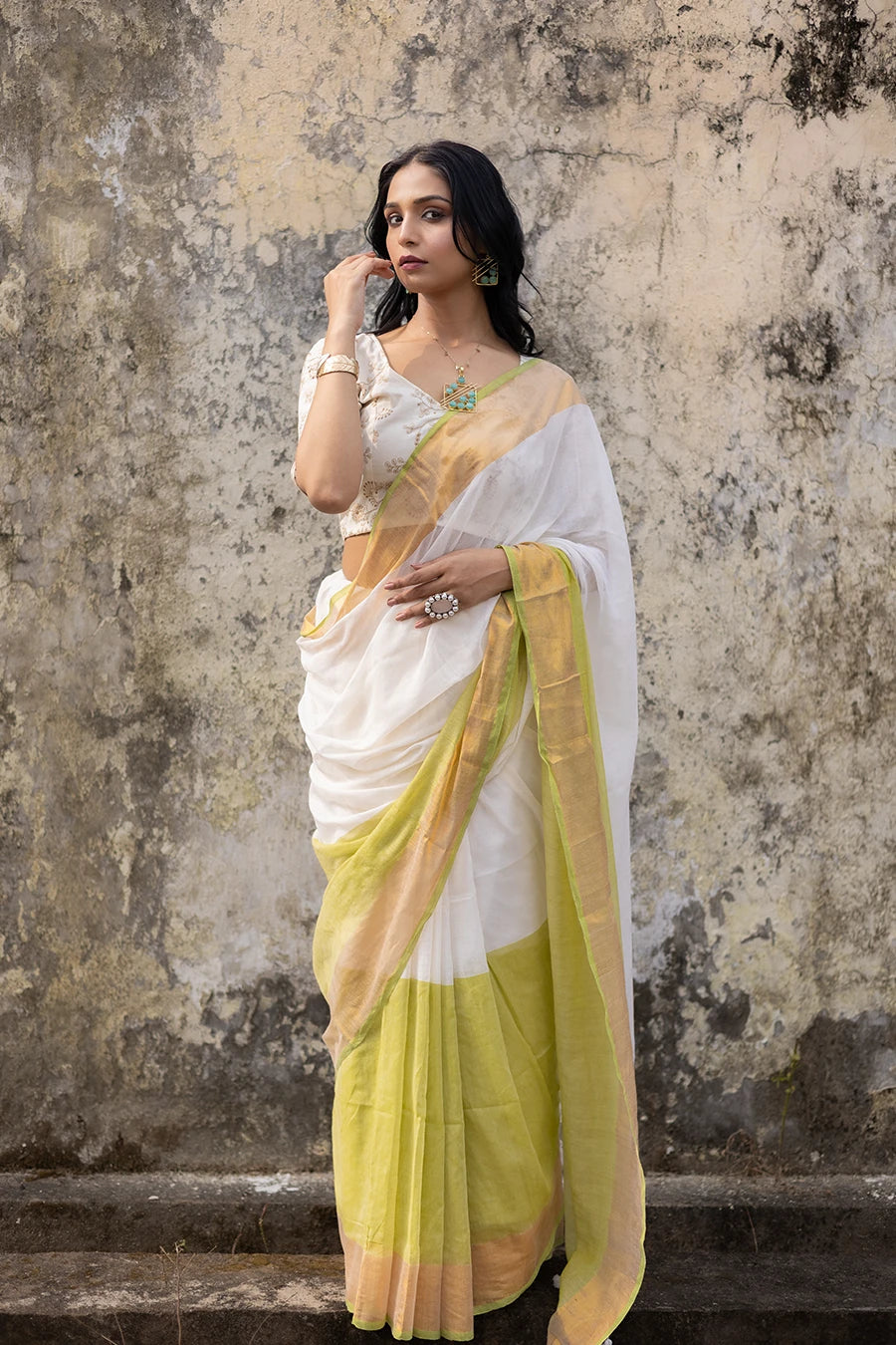 Woman wearing a white and yellow saree against a textured wall