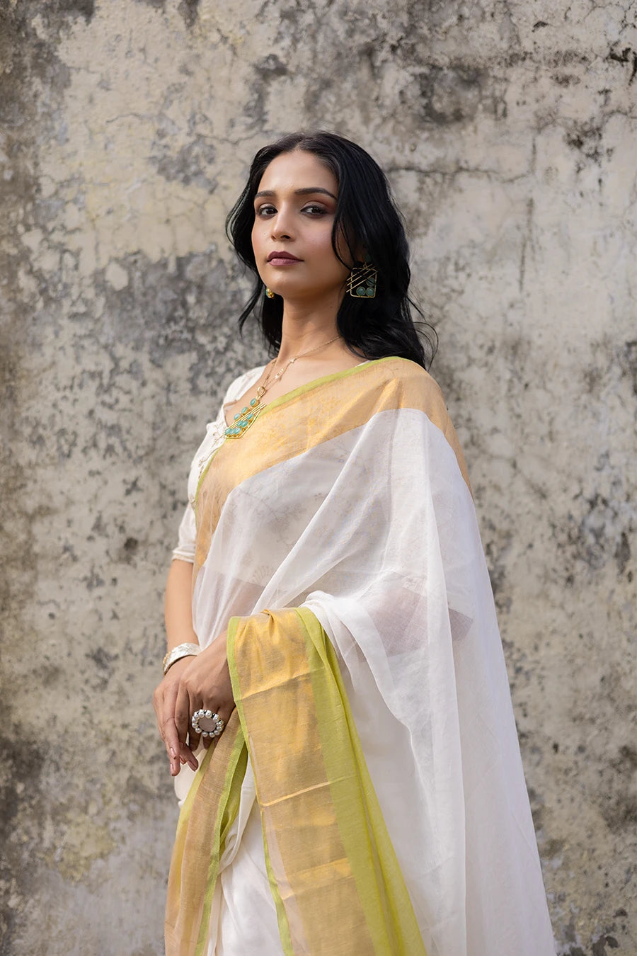 Woman wearing a white and yellow saree against a textured wall