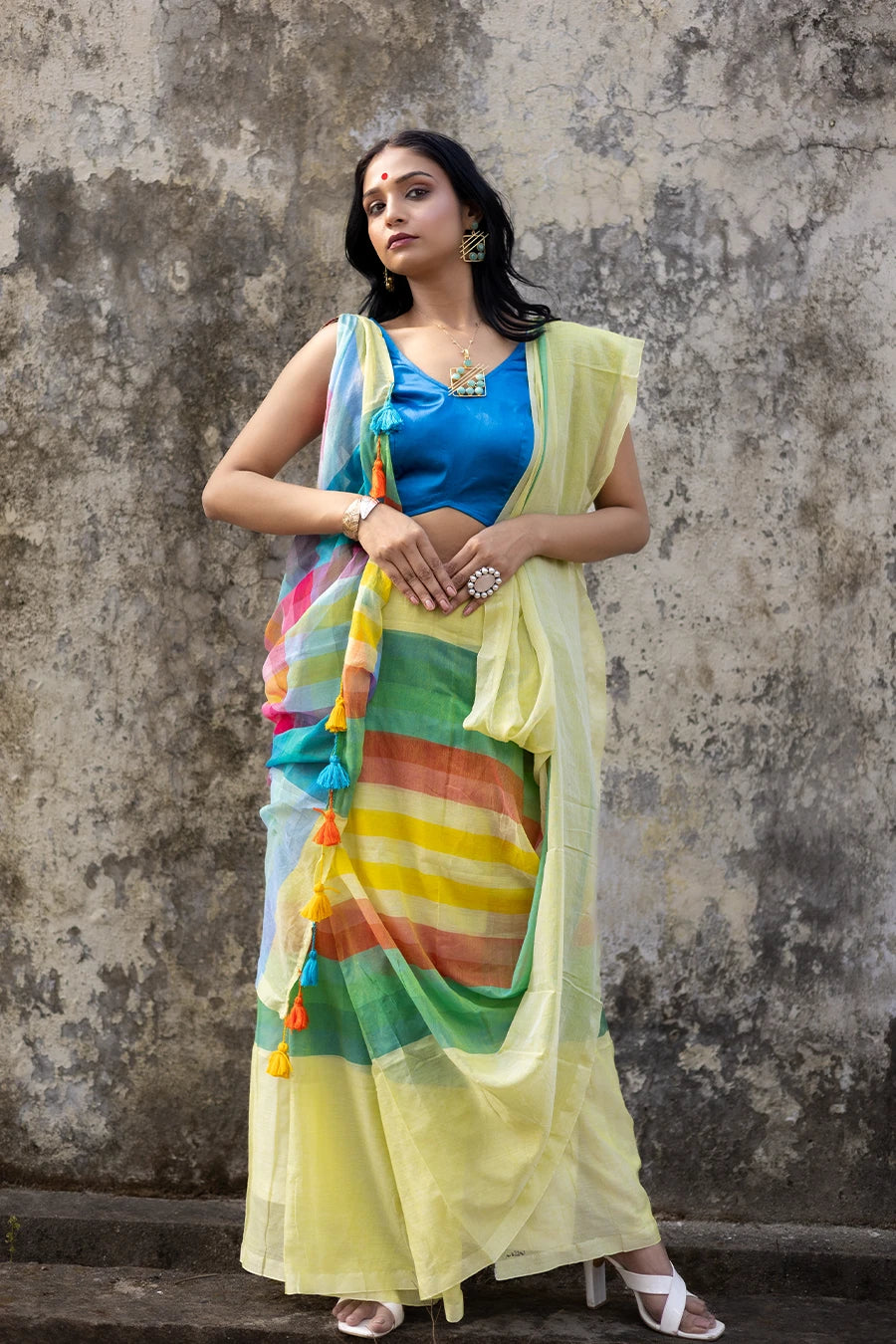 Woman wearing a colorful saree with a blue blouse against a textured wall.