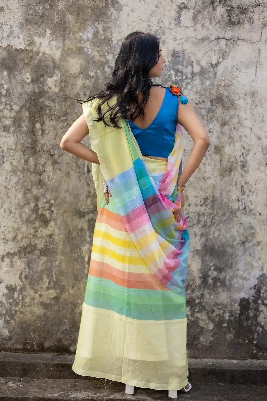 Woman wearing a colorful saree with a blue blouse against a textured wall.