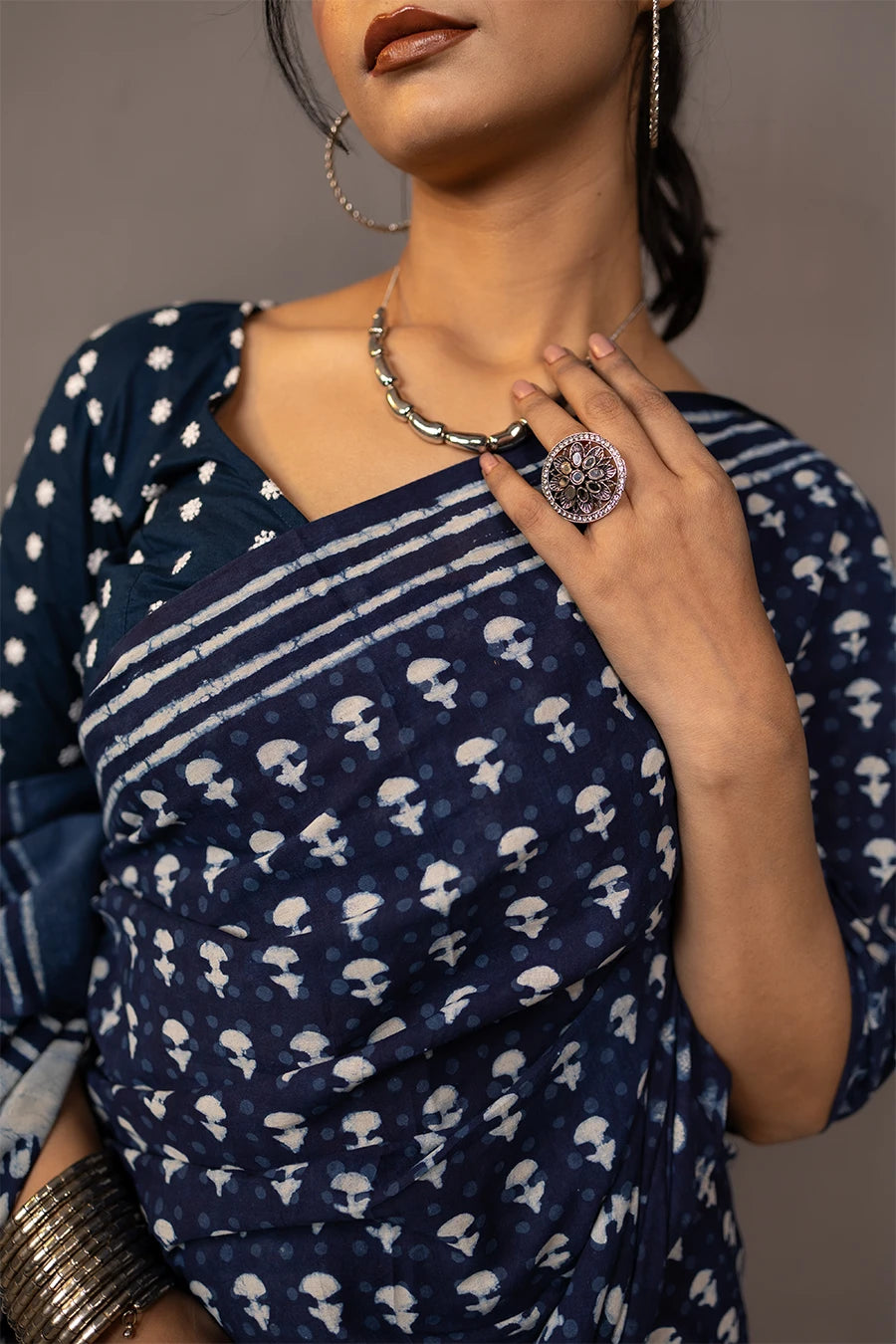 Woman wearing a blue saree with a pattern, standing next to a small table with books and a map.