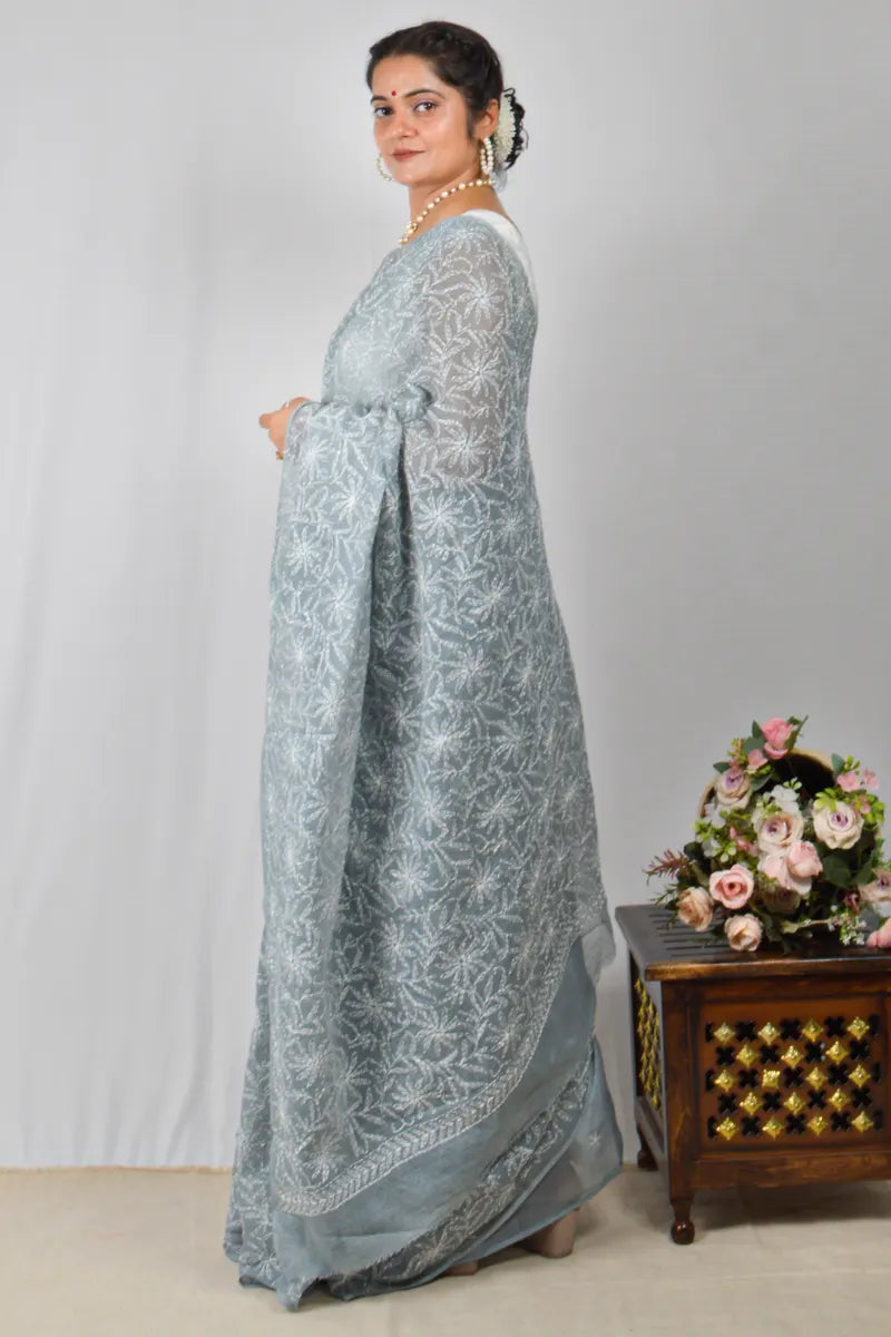 Woman in a light blue saree with a floral arrangement on a wooden table in the background