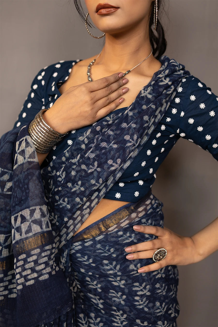 Woman in a patterned outfit standing next to a small table with books and a suitcase against a plain background