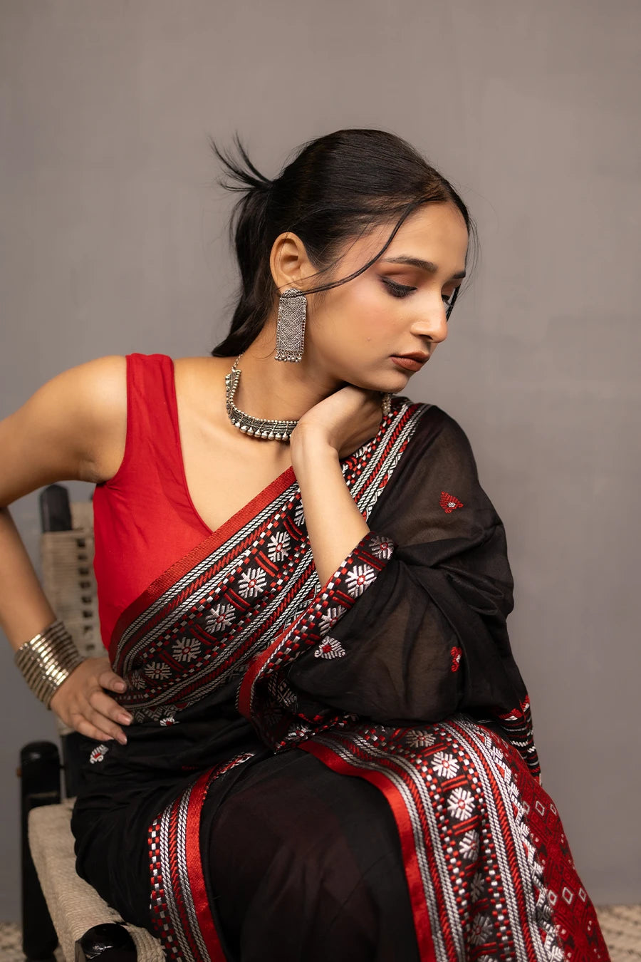Woman wearing a black and red saree with a chair in the background