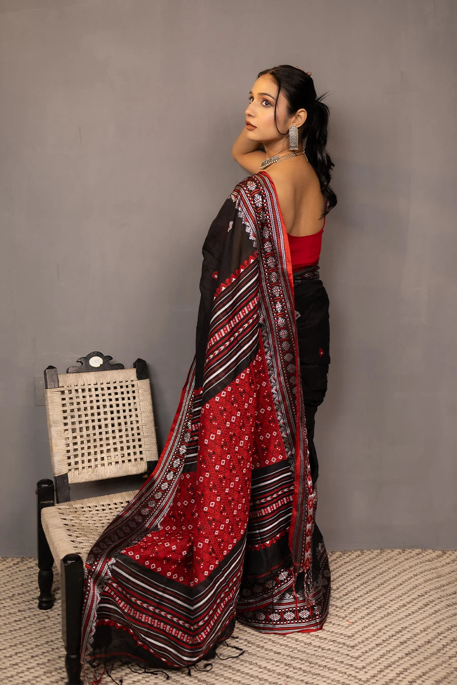 Woman wearing a black and red saree with a chair in the background