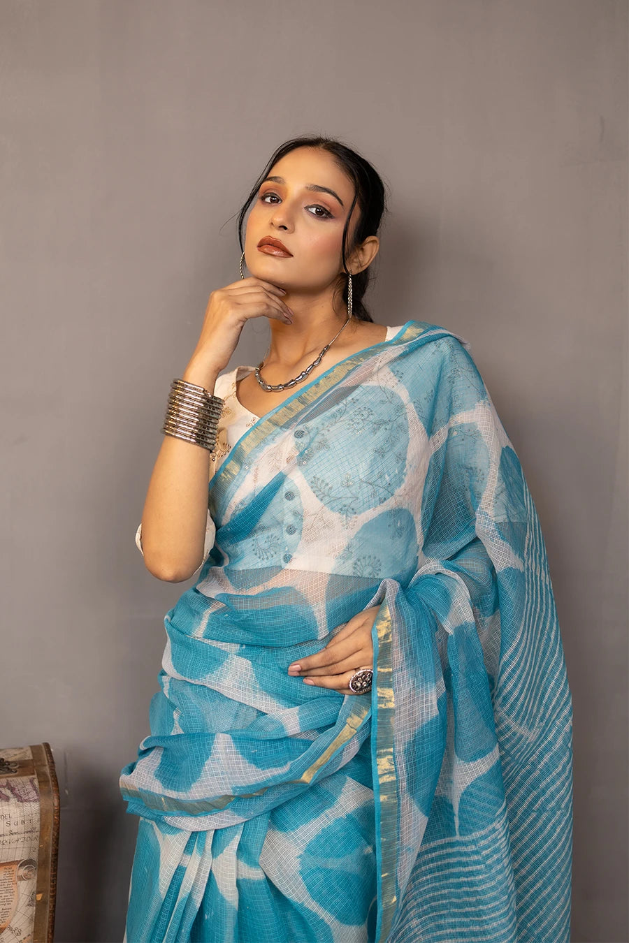 Woman in a blue saree with white patterns standing against a grey wall.