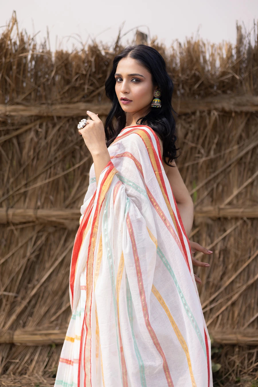 Woman in a colorful saree with tassels standing against a rustic background