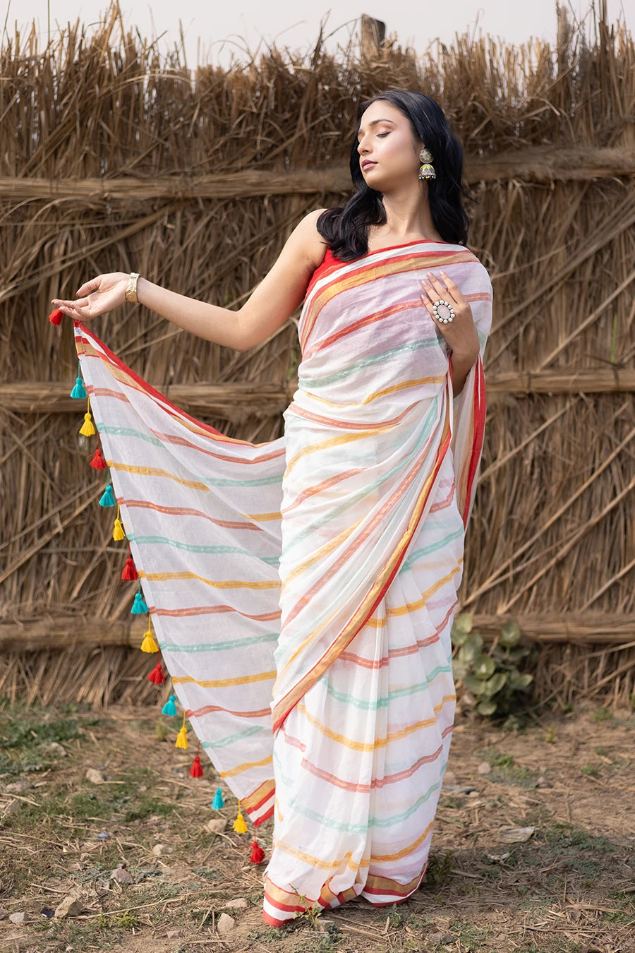 Woman in a colorful saree with tassels standing against a rustic background