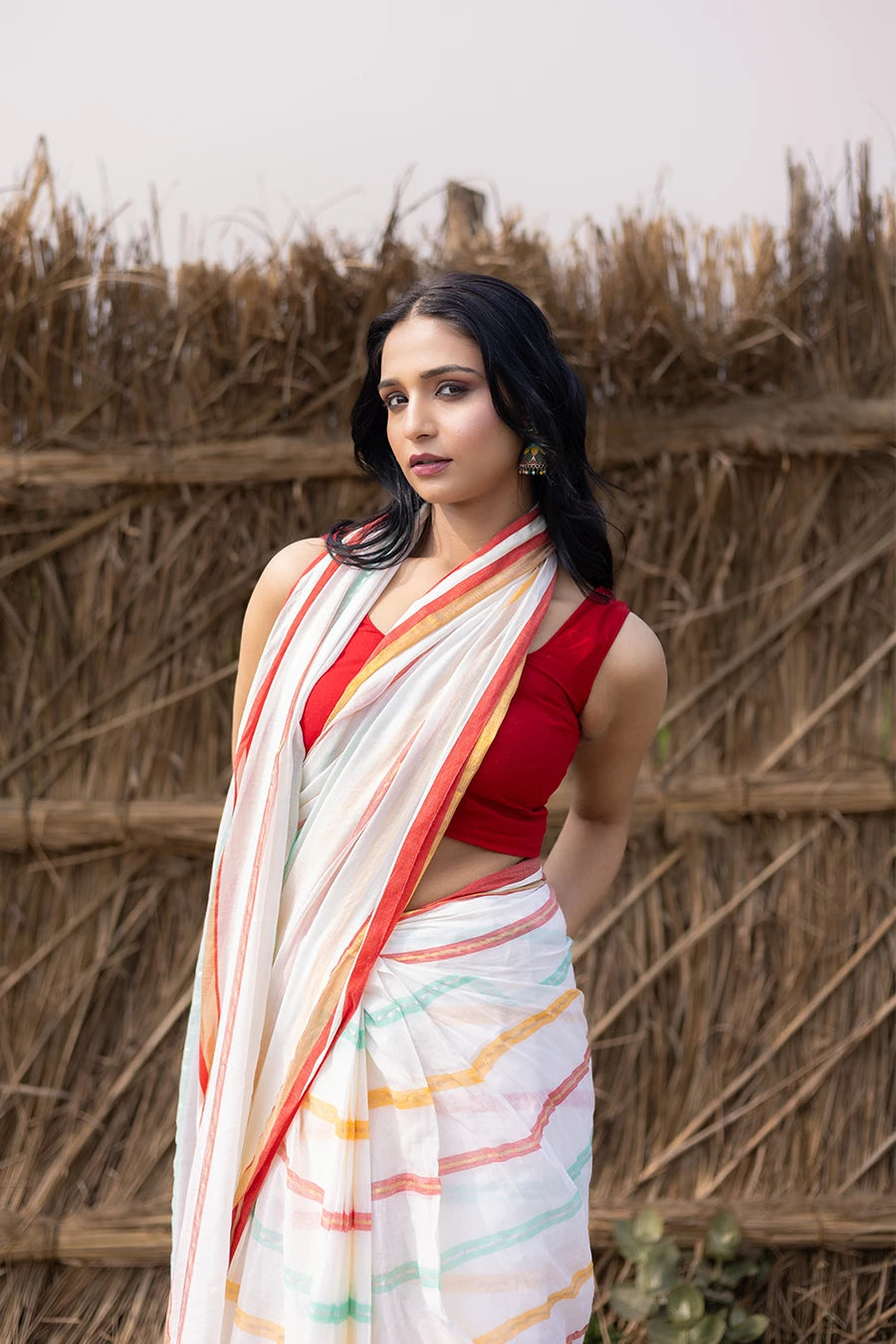 Woman in a colorful saree with tassels standing against a rustic background