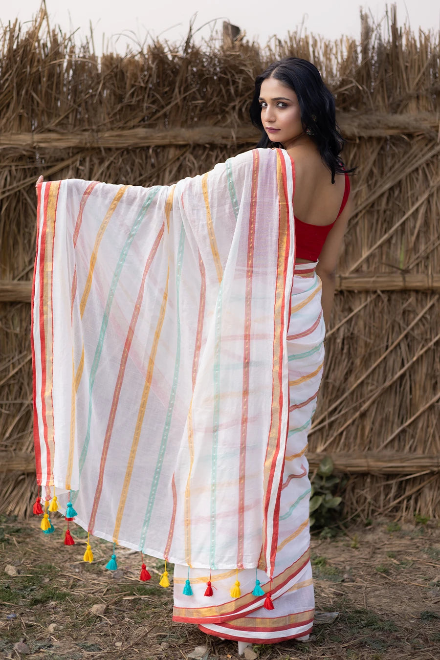Woman in a colorful saree with tassels standing against a rustic background