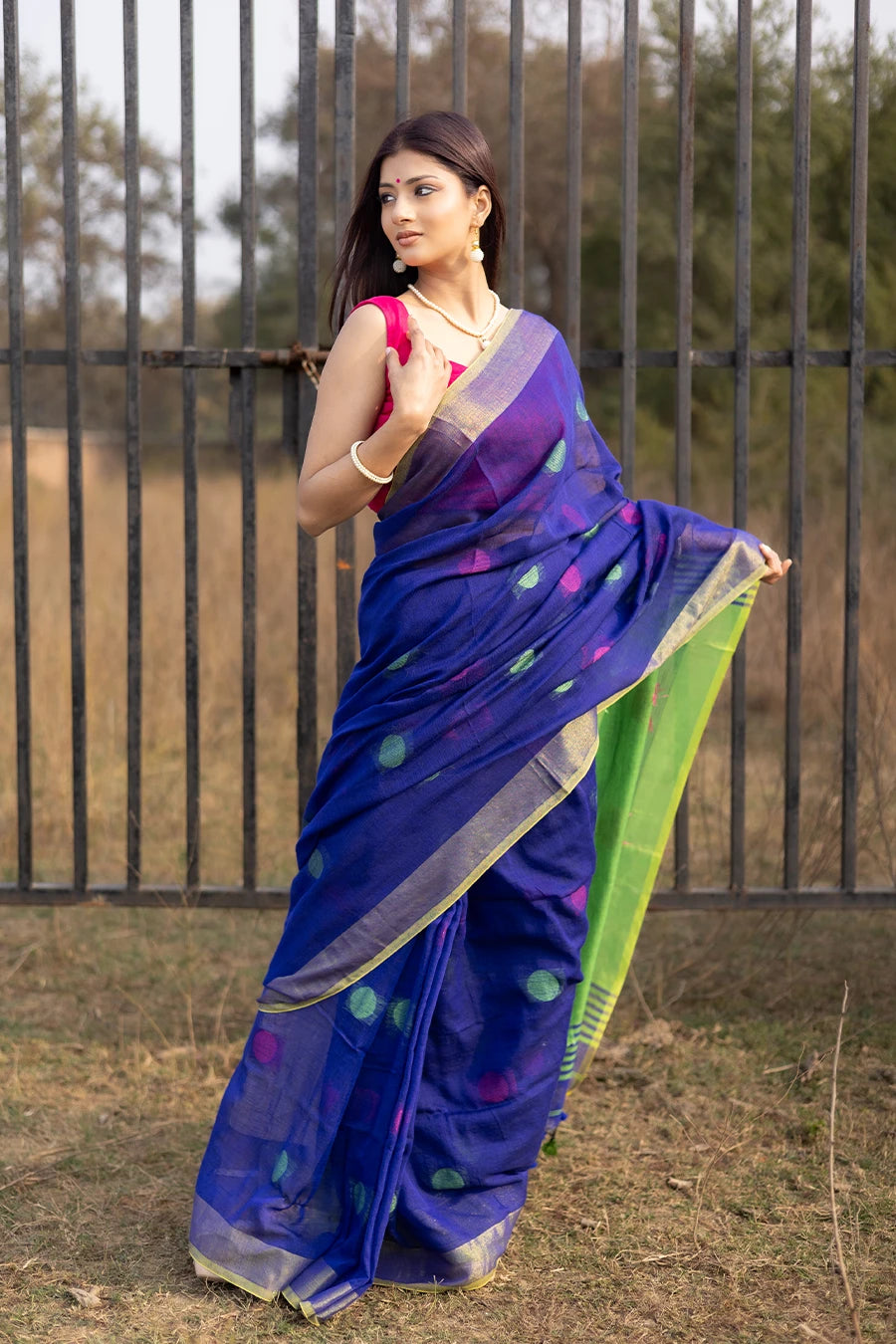 Woman wearing a blue and green saree with a pink blouse, standing outdoors.