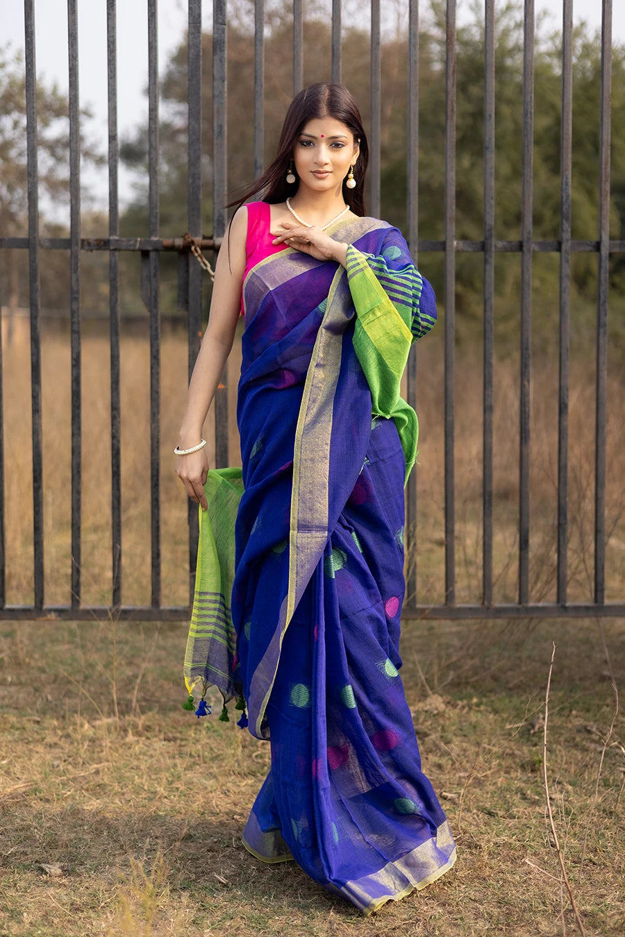 Woman wearing a blue and green saree with a pink blouse, standing outdoors.