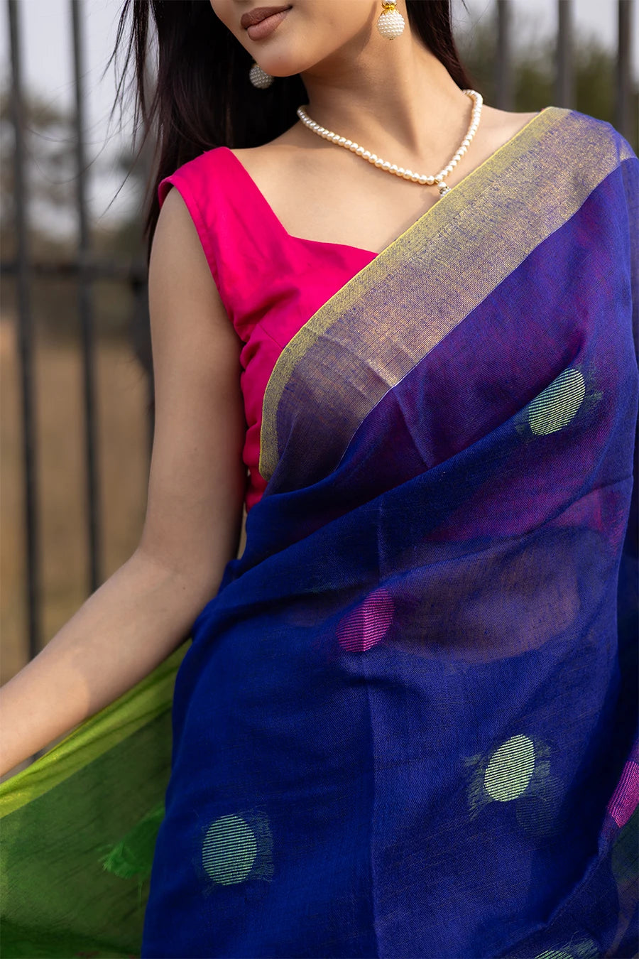 Woman wearing a blue and green saree with a pink blouse, standing outdoors.