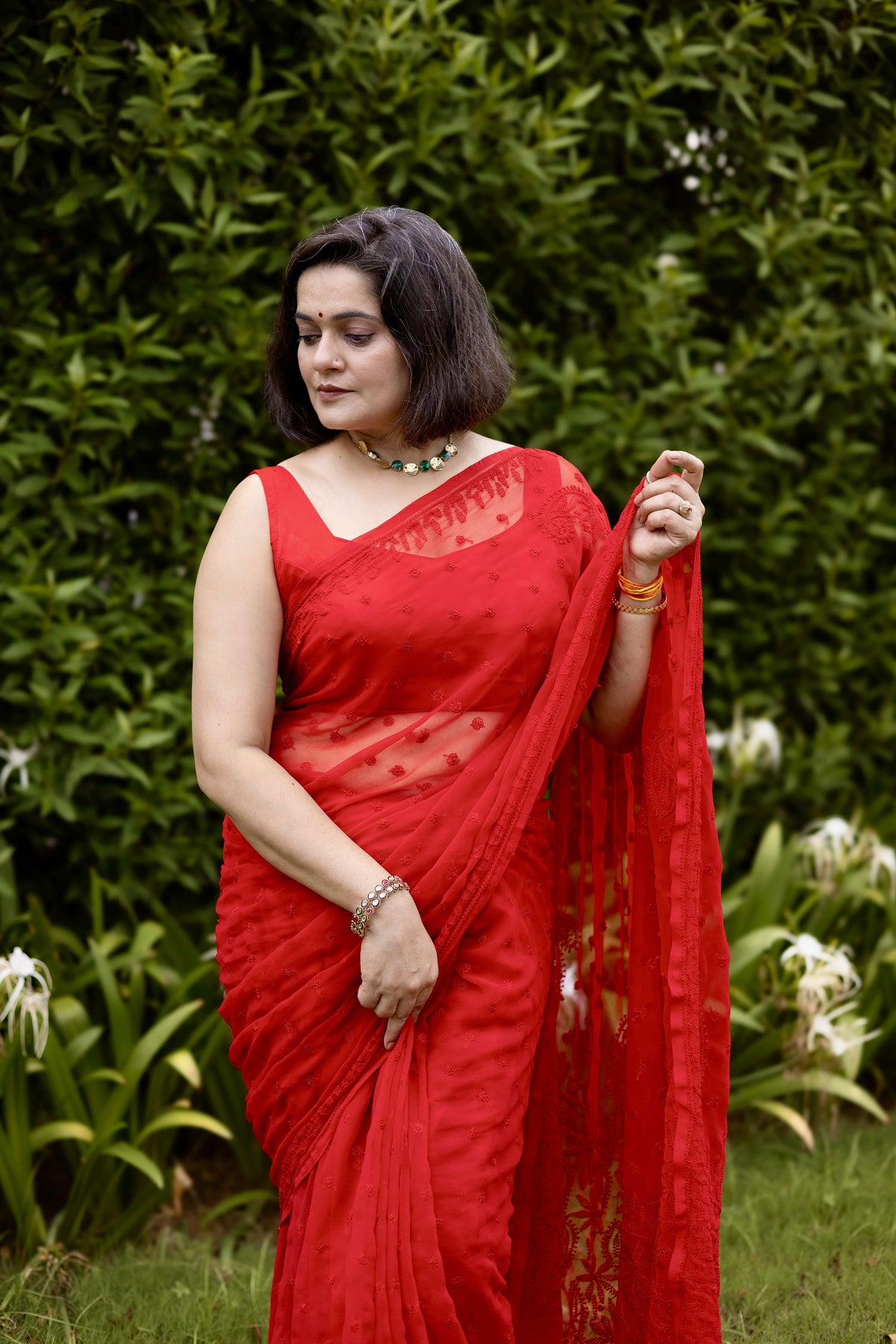 Front view of woman in red georgette chikankari saree with blouse, holding pallu