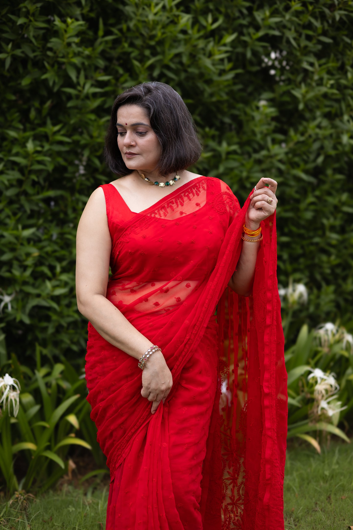 Front view of woman in red georgette chikankari saree with blouse, holding pallu