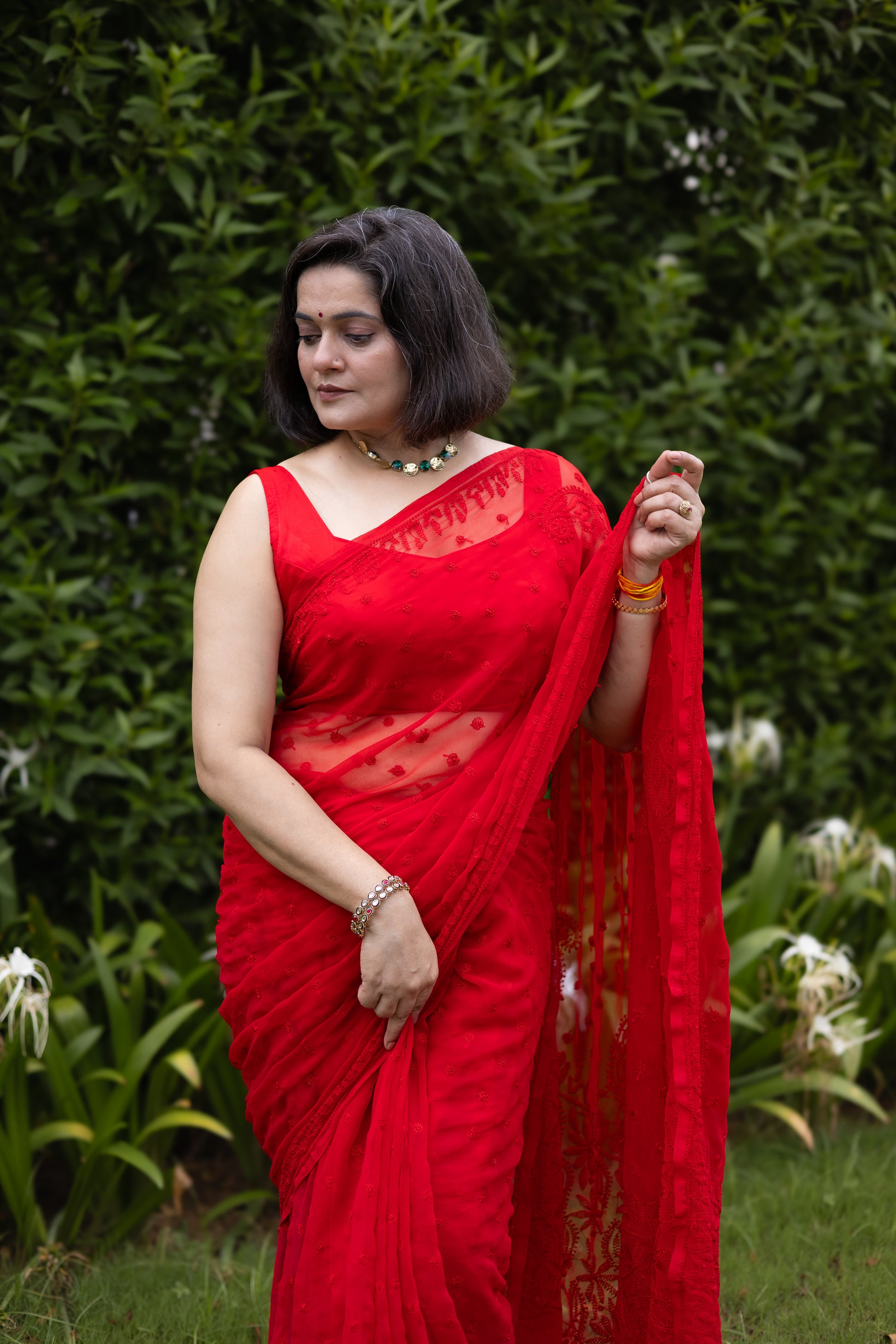 Front view of woman in red georgette chikankari saree with blouse, holding pallu