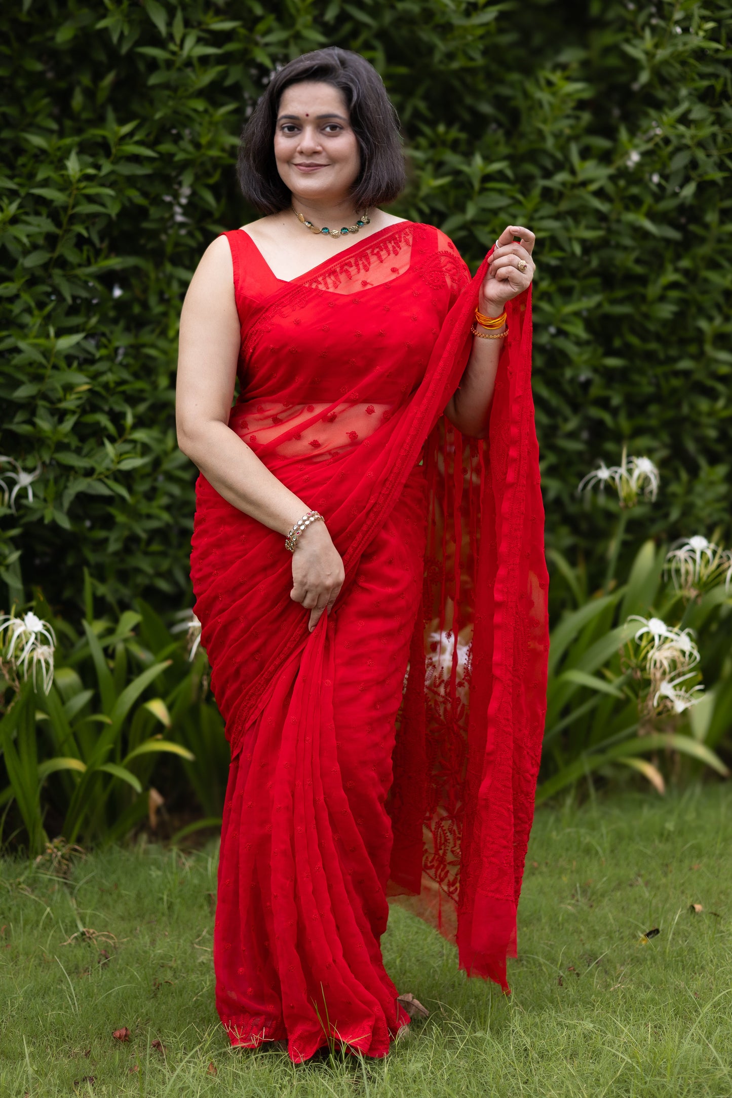 Woman wearing red georgette Lucknowi chikankari saree with blouse, front pose in garden