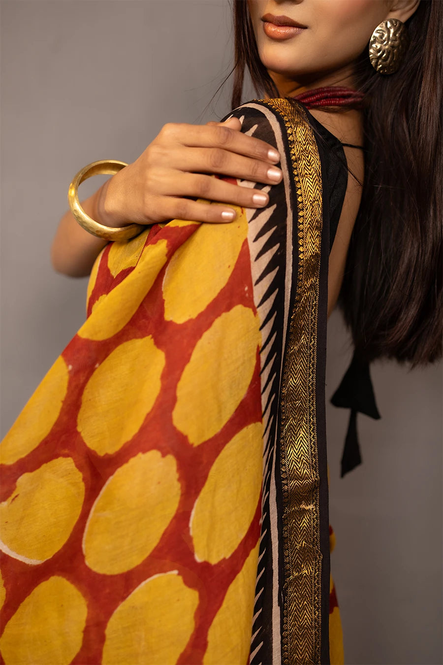 Woman wearing a traditional saree with a patterned design, standing next to a small table with books and a suitcase.