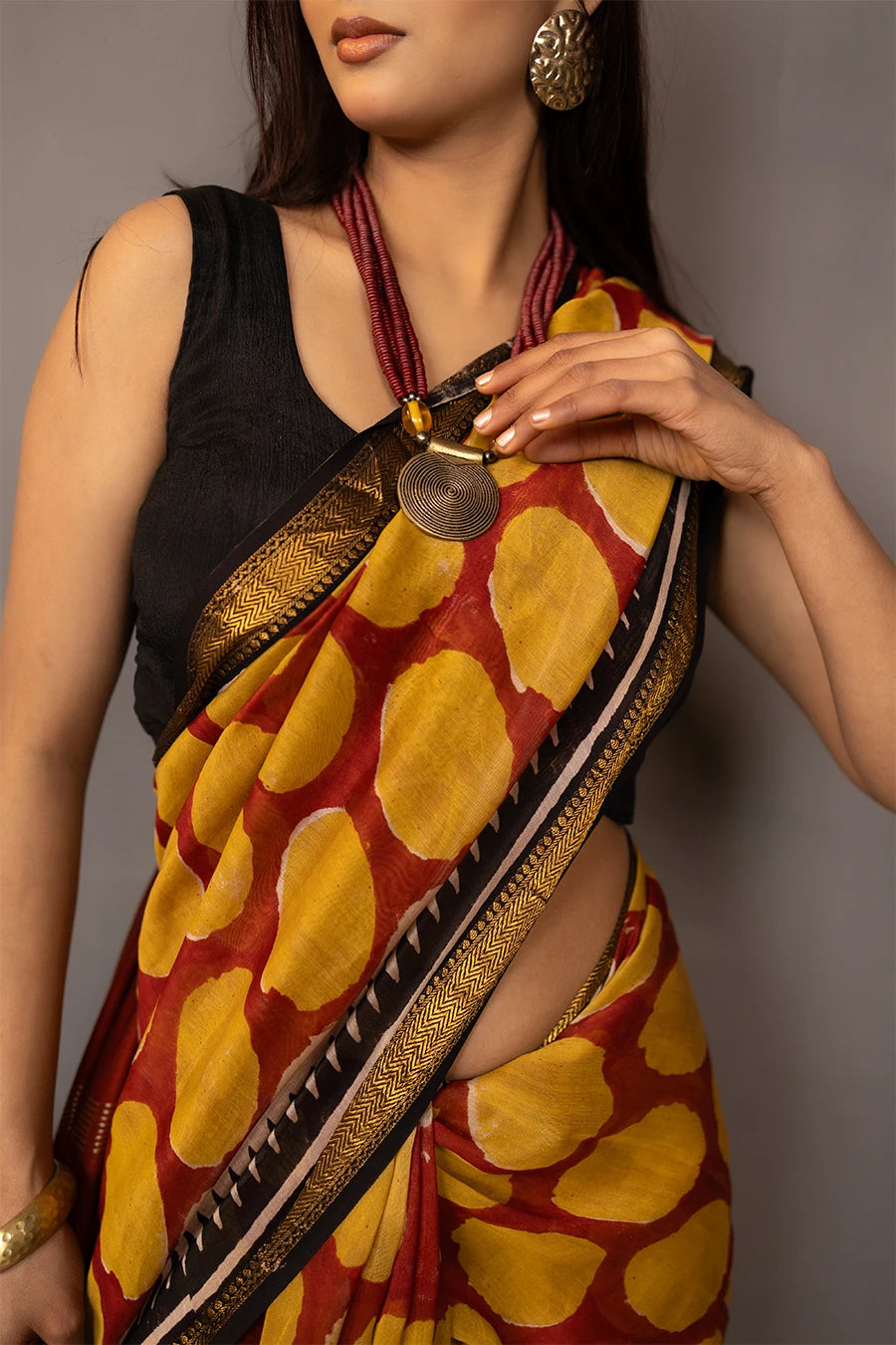 Woman wearing a traditional saree with a patterned design, standing next to a small table with books and a suitcase.