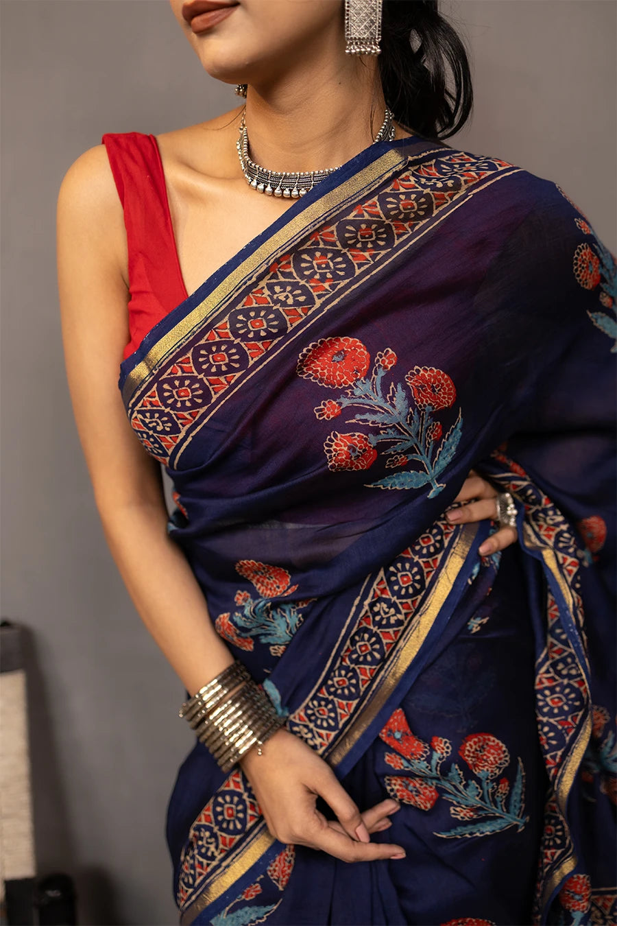 Woman wearing a blue saree with a red blouse against a grey background