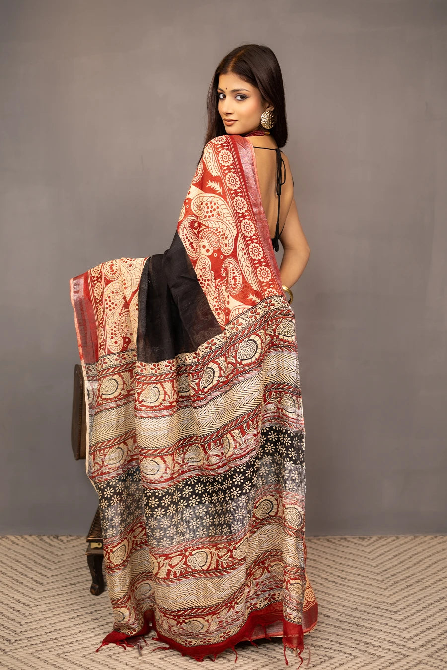 Woman wearing a traditional saree with a patterned design, standing next to a small table with books and a suitcase.