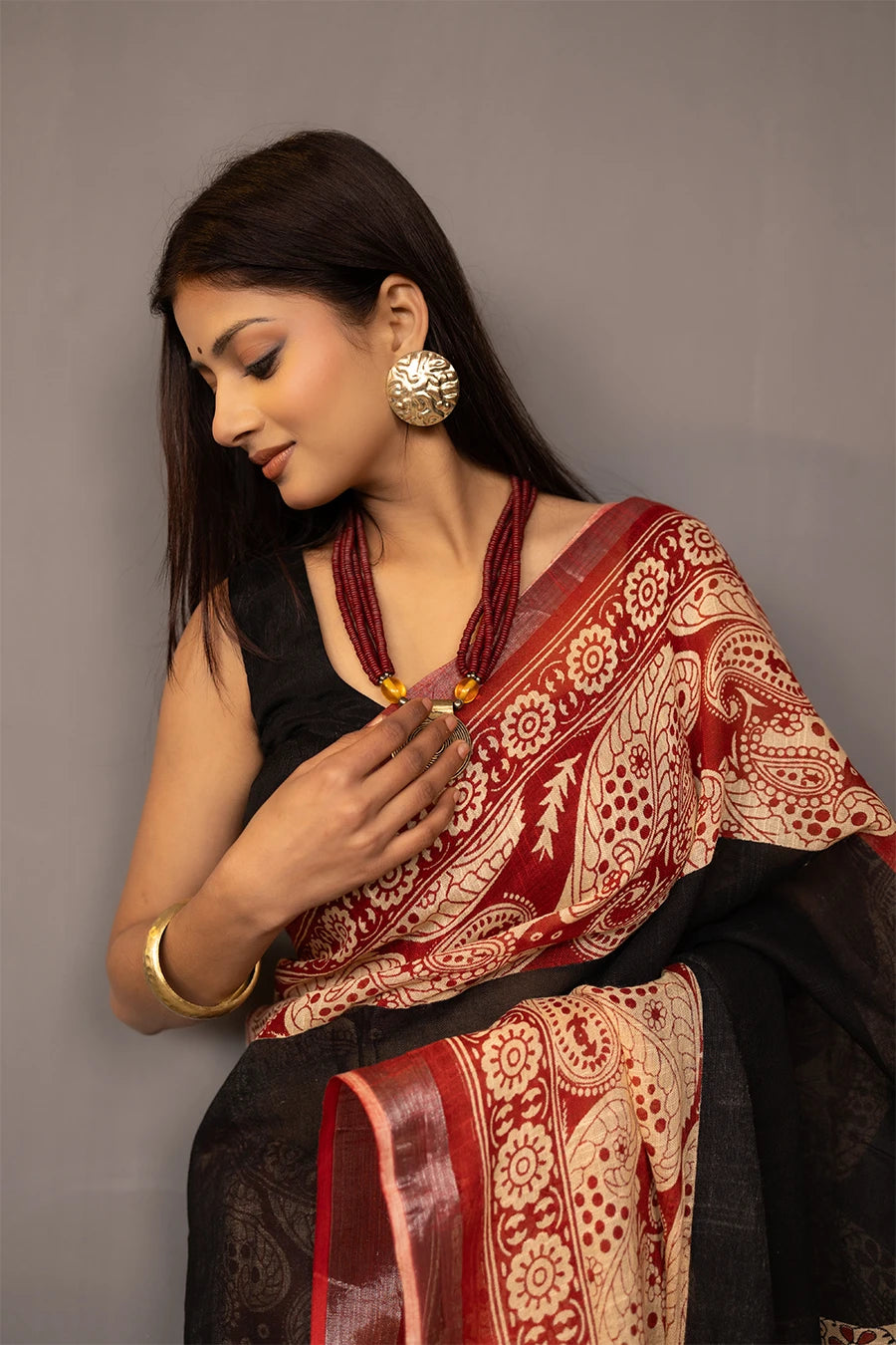 Woman wearing a traditional saree with a patterned design, standing next to a small table with books and a suitcase.