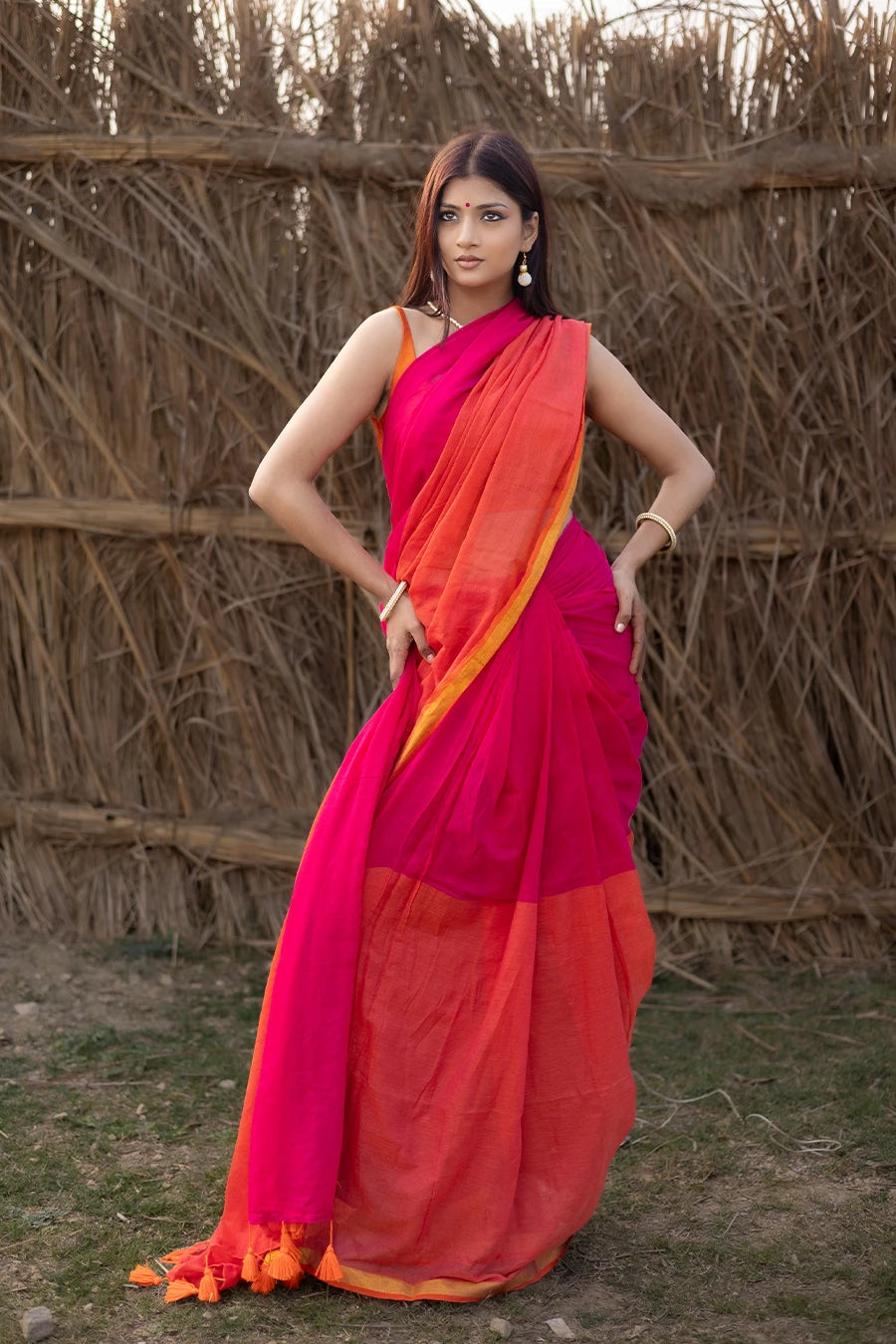 Model wearing a magenta and orange mul cotton saree with contrast border and tassel detailing, suitable for daily wear, casual outings, and festive occasions.