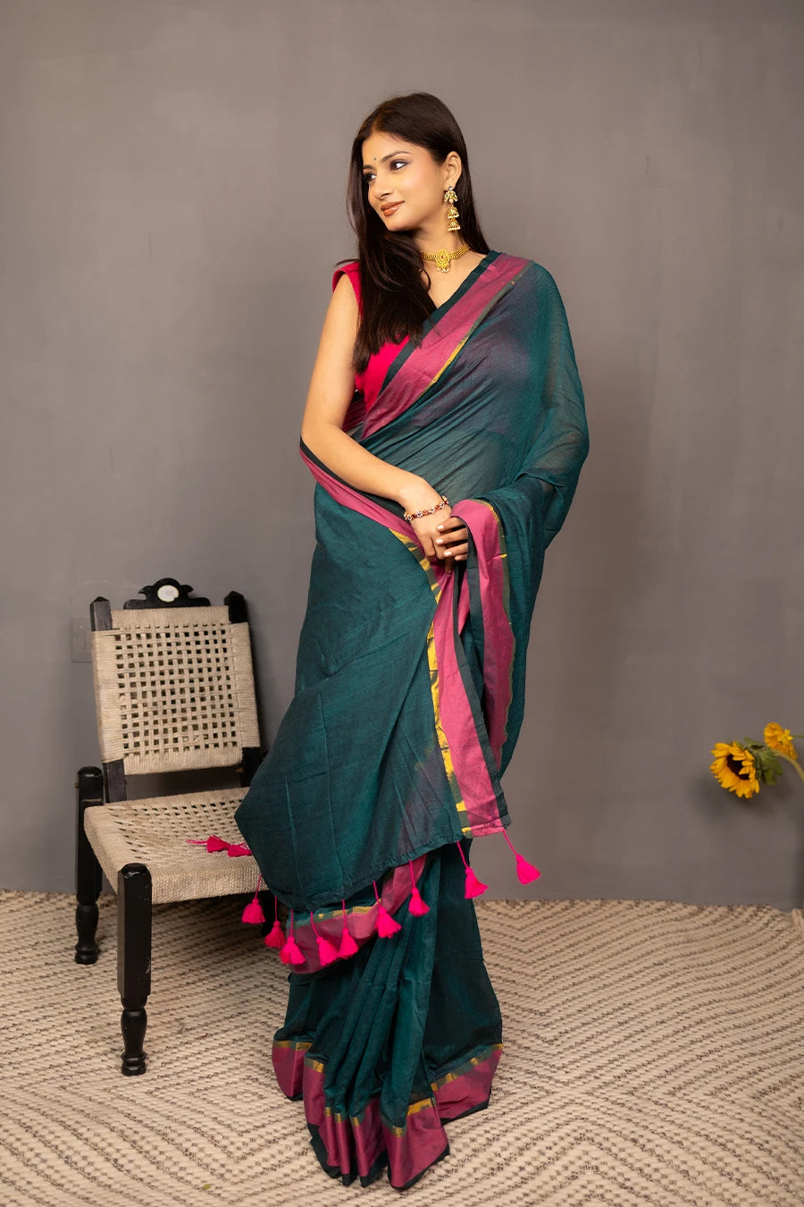 Woman holding a teal saree with pink border against a grey background