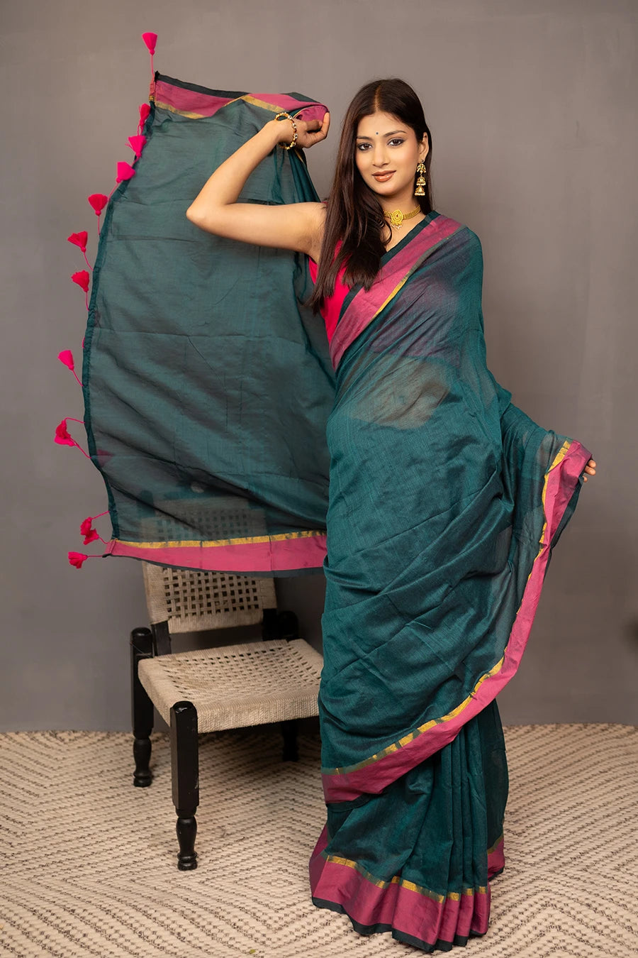 Woman holding a teal saree with pink border against a grey background
