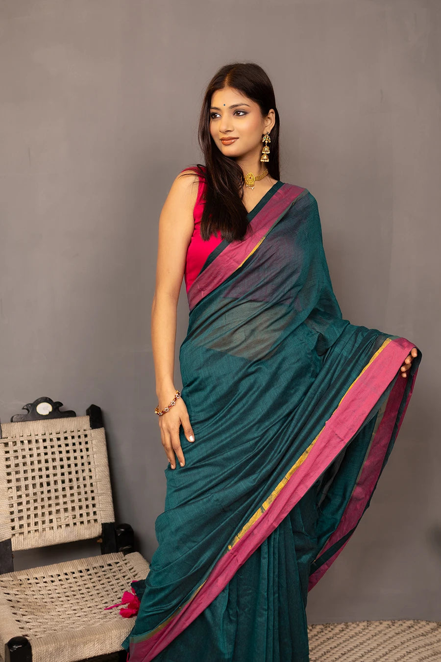 Woman holding a teal saree with pink border against a grey background