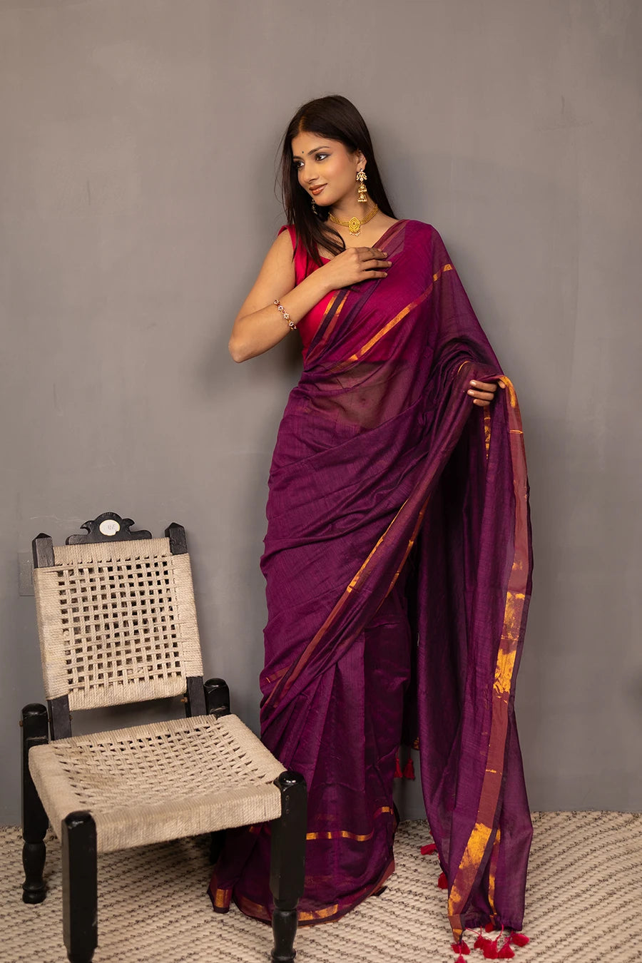 Woman wearing a purple saree with a red blouse against a grey background
