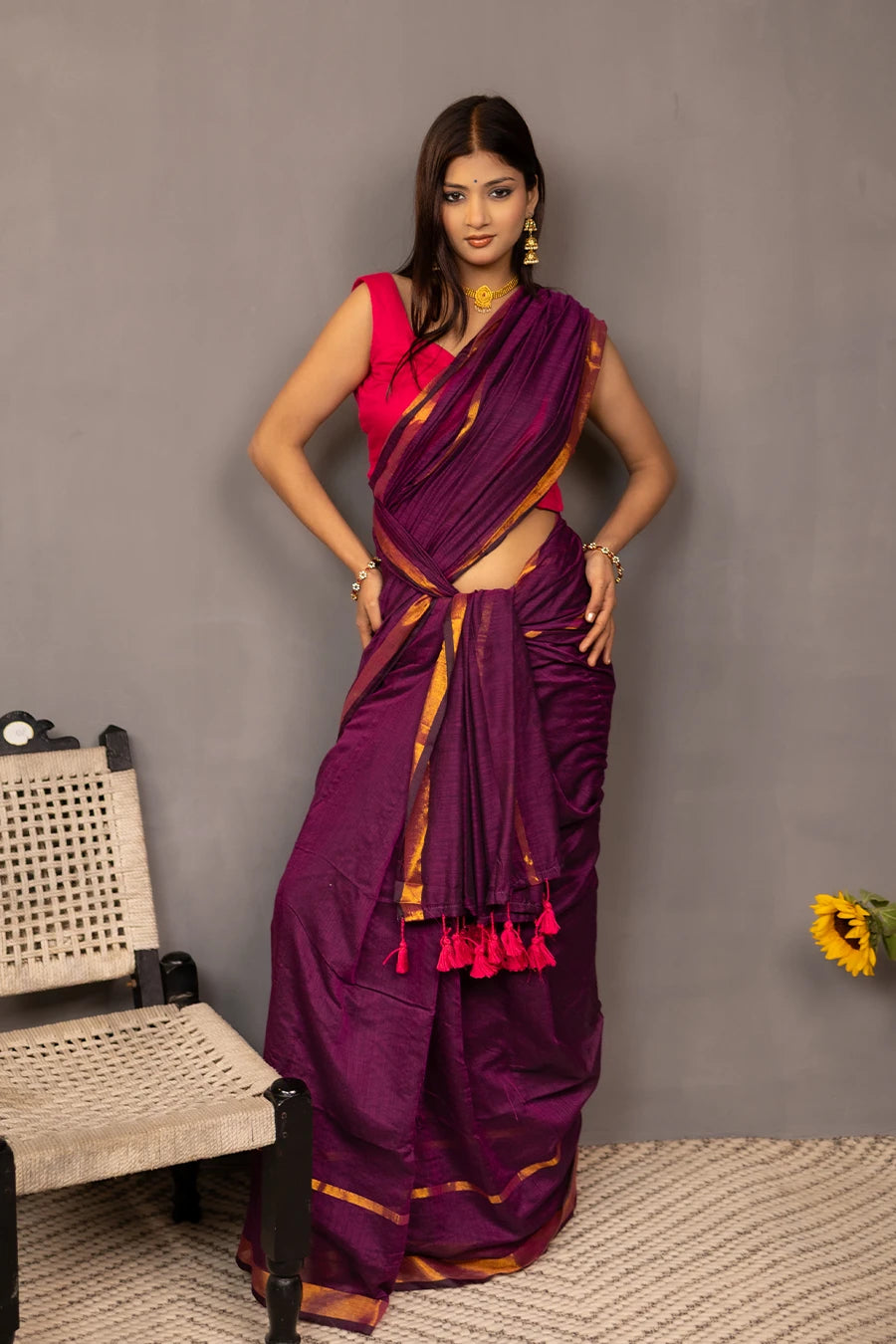 Woman wearing a purple saree with a red blouse against a grey background