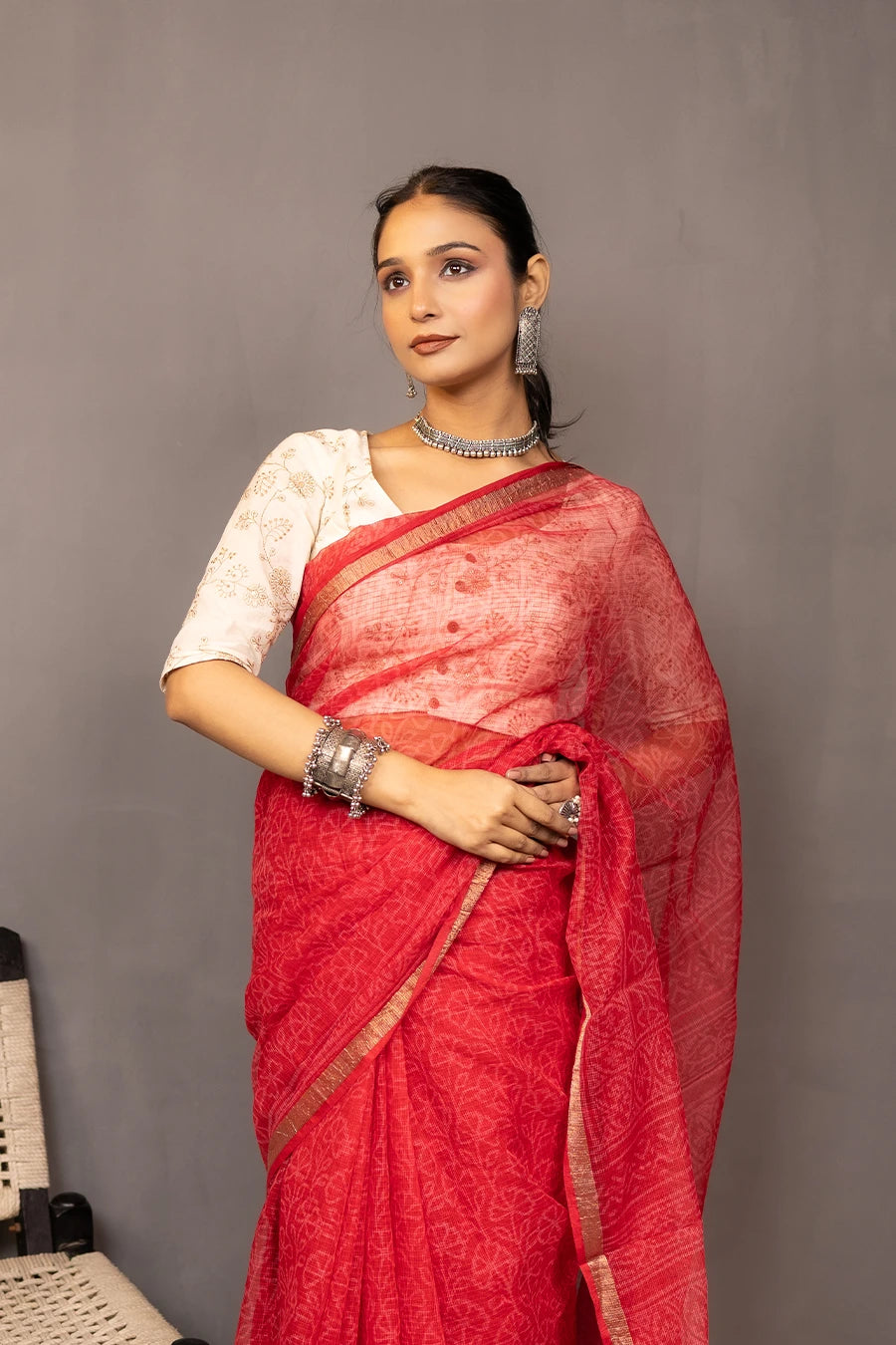 Woman wearing a red saree with a white blouse against a grey background