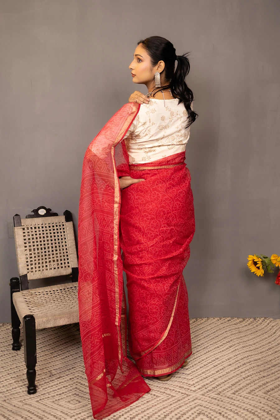 Woman wearing a red saree with a white blouse against a grey background