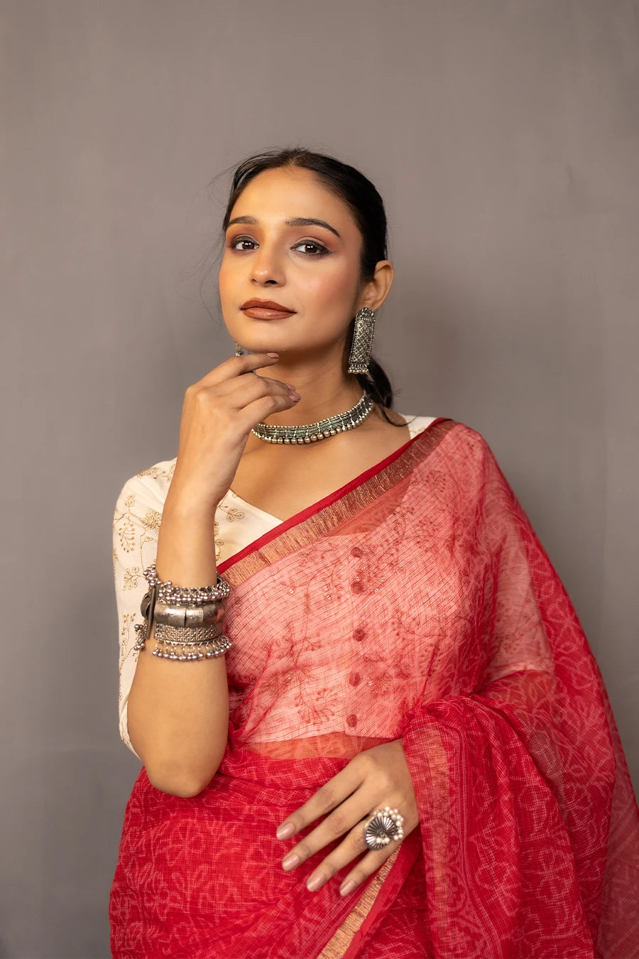 Woman wearing a red saree with a white blouse against a grey background