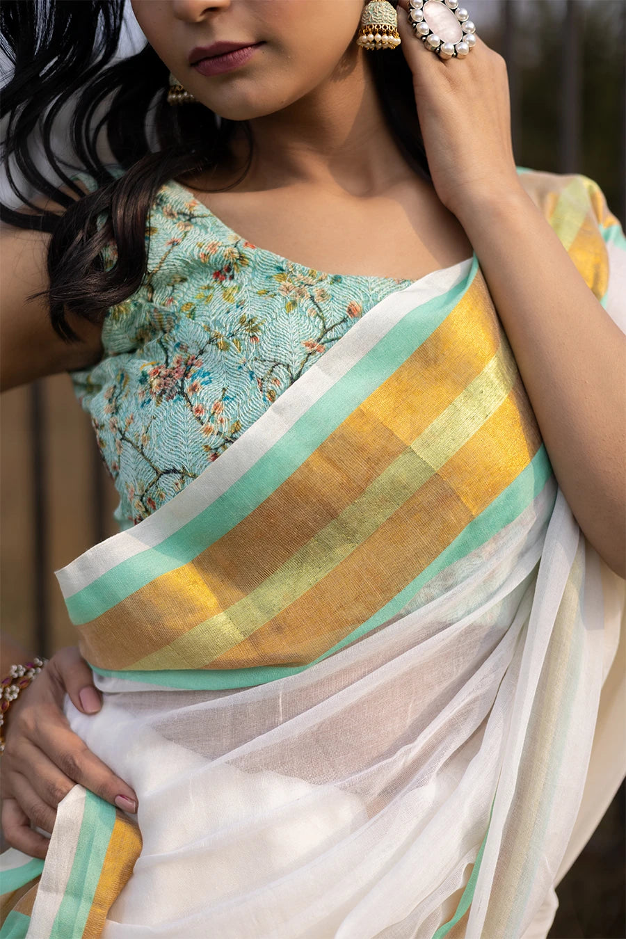 Model wearing an off-white saree with gold and mint green striped border and tassel detailing, lightweight and suitable for festive and casual occasions.