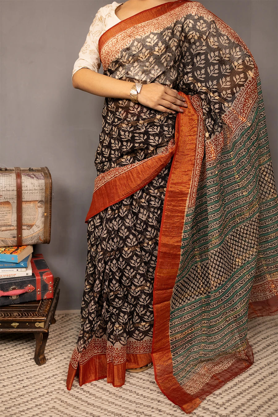 Woman wearing a traditional saree with a patterned design, standing next to vintage suitcases on a textured surface.