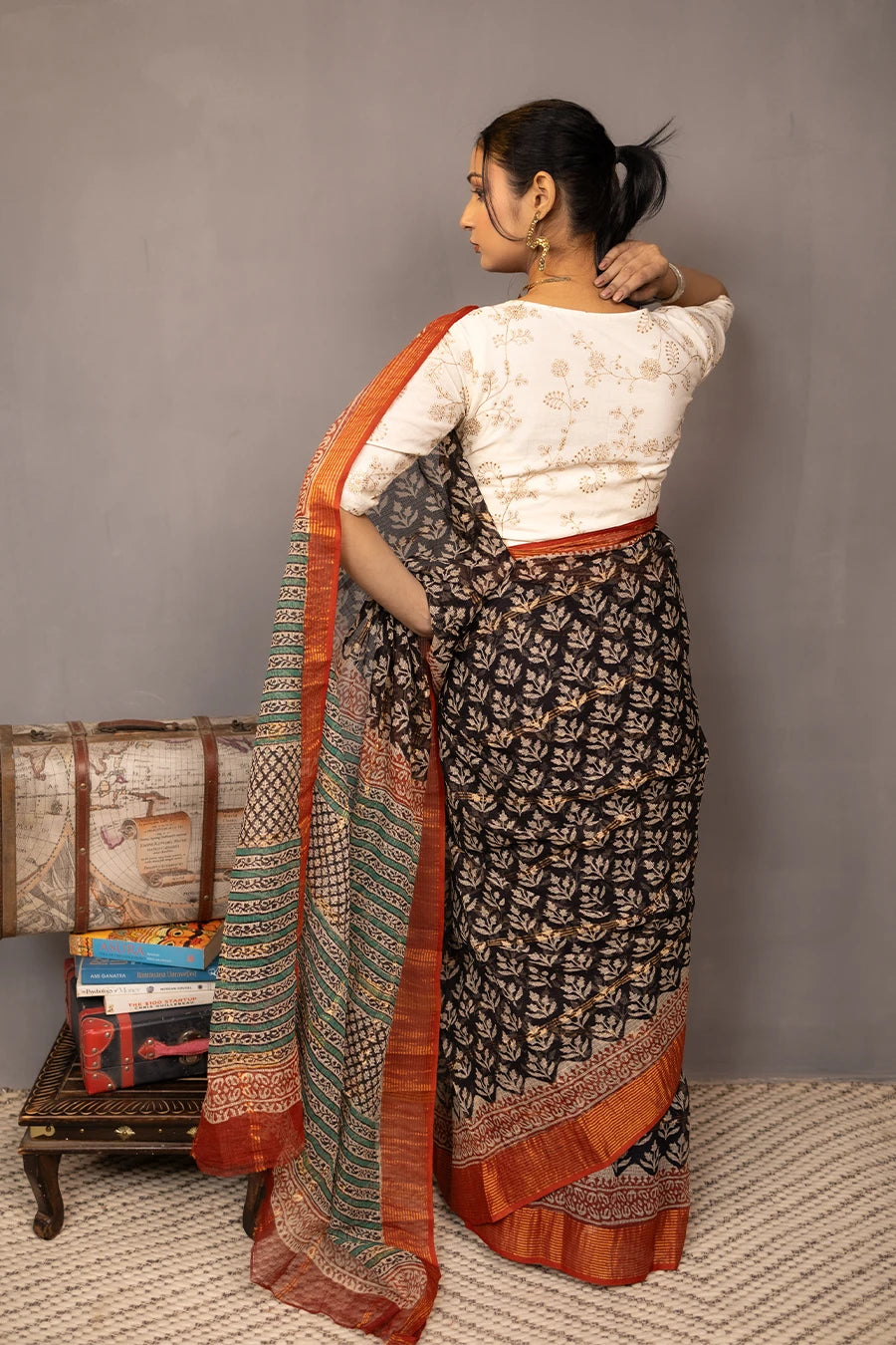 Woman wearing a traditional saree with a patterned design, standing next to vintage suitcases on a textured surface.