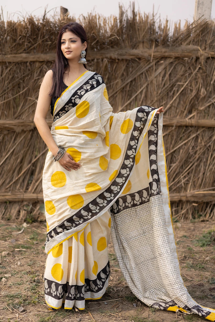 Woman wearing a traditional saree with yellow and white pattern in front of a rustic background