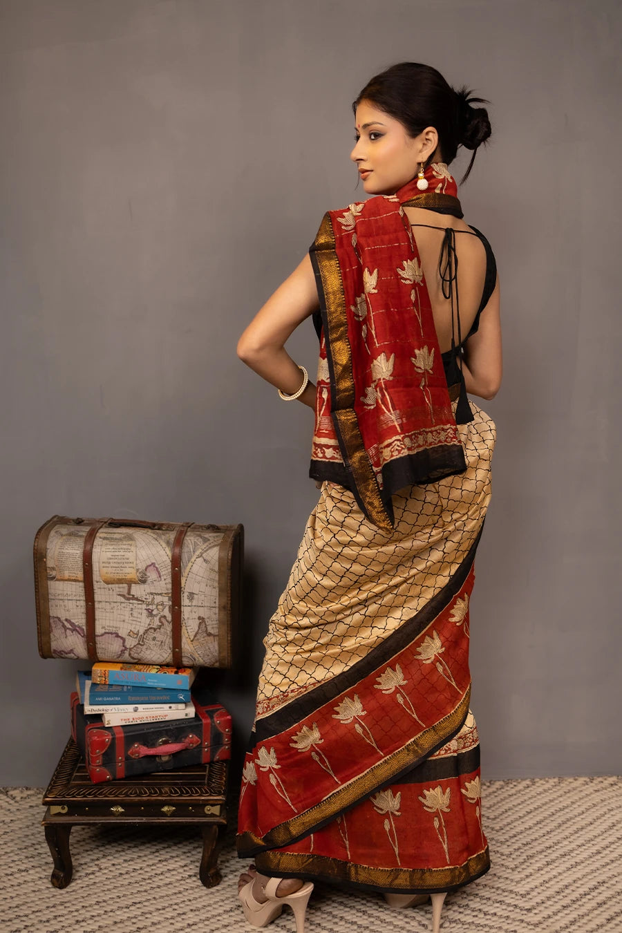 Woman wearing a traditional saree with a red border, standing next to a small table with books and a map.