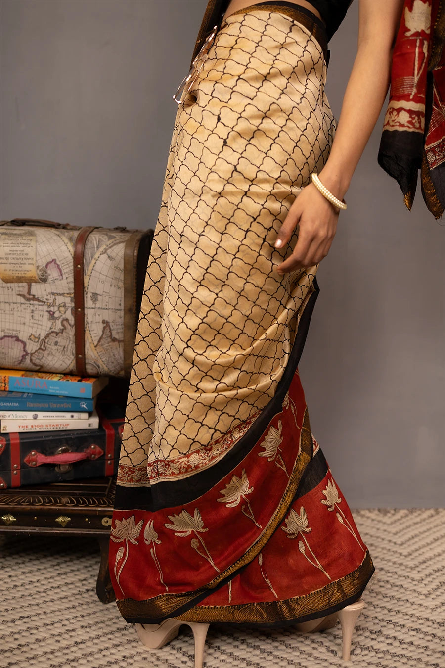 Woman wearing a traditional saree with a red border, standing next to a small table with books and a map.