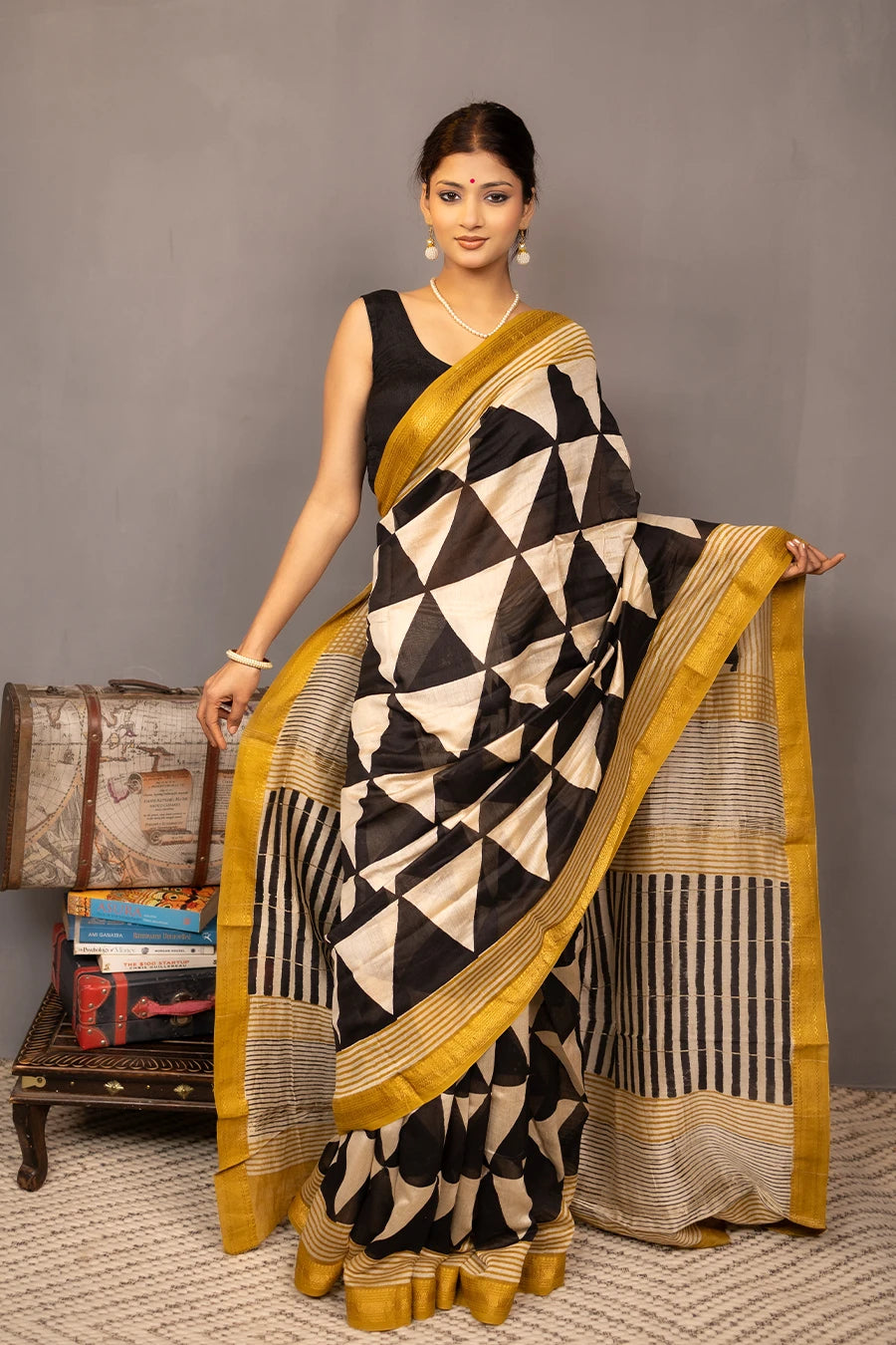 Woman wearing a black and white patterned saree with gold border, standing against a grey background.
