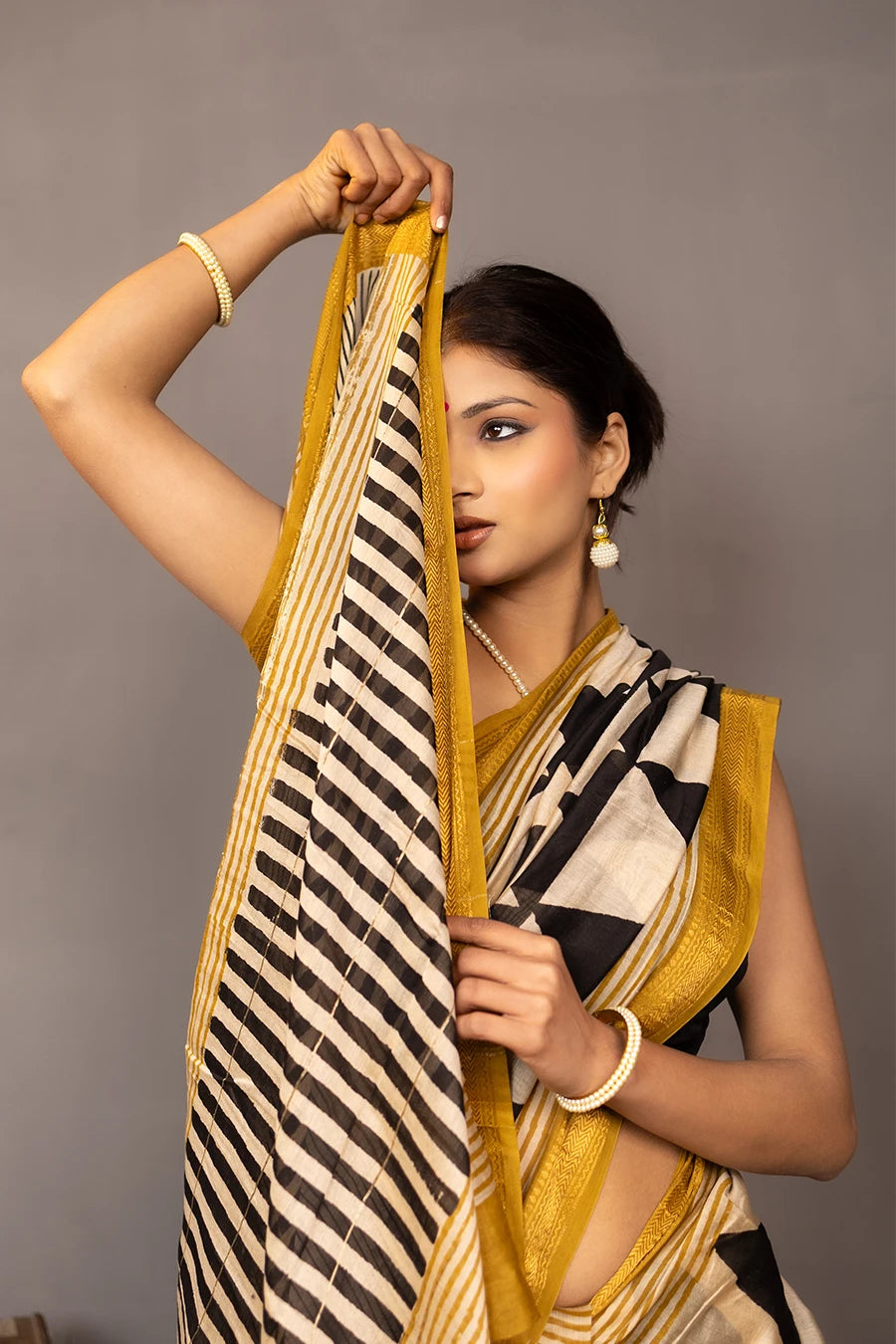 Woman wearing a black and white patterned saree with gold border, standing against a grey background.