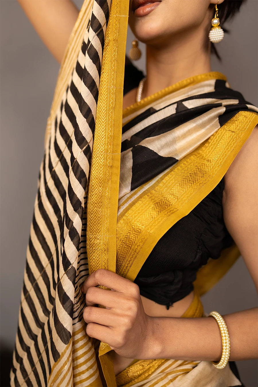 Woman wearing a black and white patterned saree with gold border, standing against a grey background.