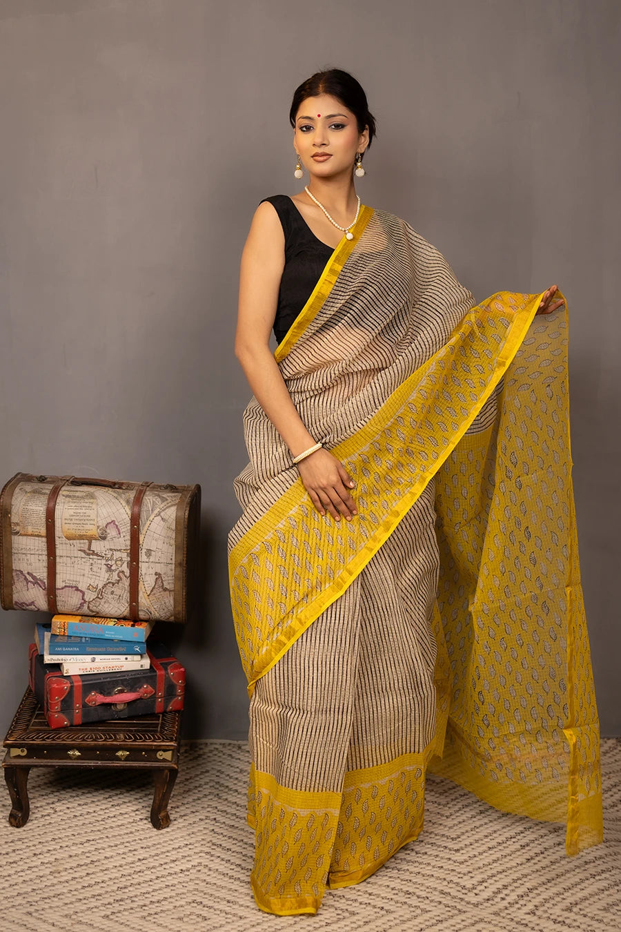 Woman wearing a beige and yellow saree with a grey background