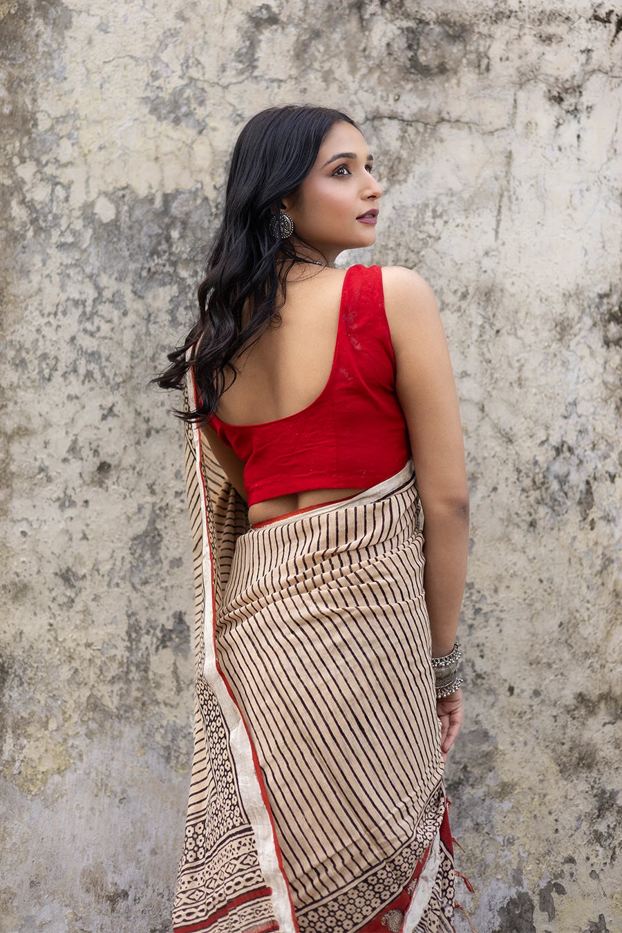 Woman in a red and beige saree standing on steps with a textured wall background