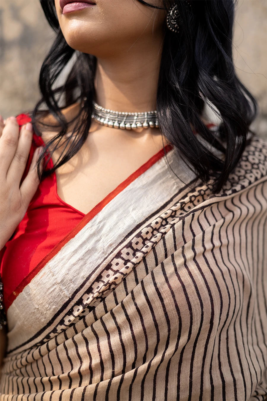 Woman in a red and beige saree standing on steps with a textured wall background